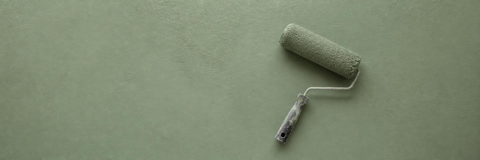 Paint roller resting on a freshly painted sage green wall